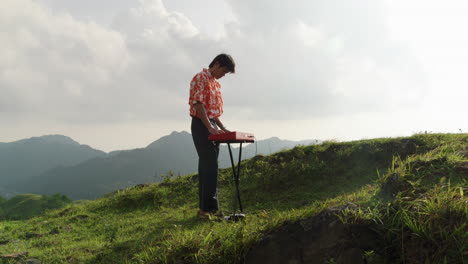 slow motion clip of a man playing the piano outside on a hilltop