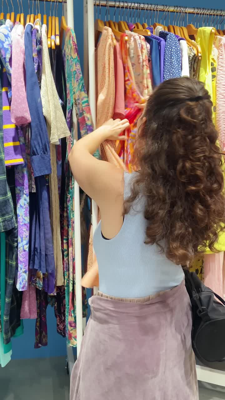 Female looking for second hand clothes and stylish used items on sale in boutique shop or flea market. Young woman browsing clothes on hanger in charity donation retail store. Zero waste influencer