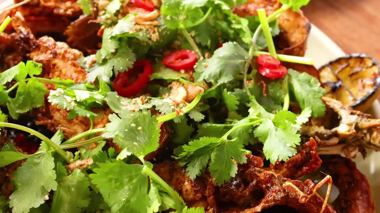 Close-up of a lobster dish garnished with cilantro, grilled lime, and red chili slices on a wooden table.