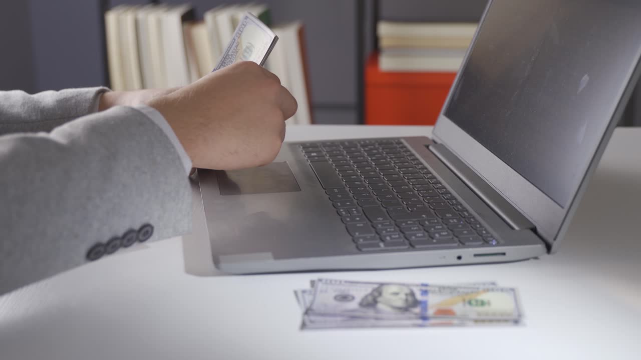 노트북에서 일하는 남자가 달러를 세고 있습니다.