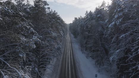 aerial view of a snowy forest road in lithuania during winter with distant cars approaching
