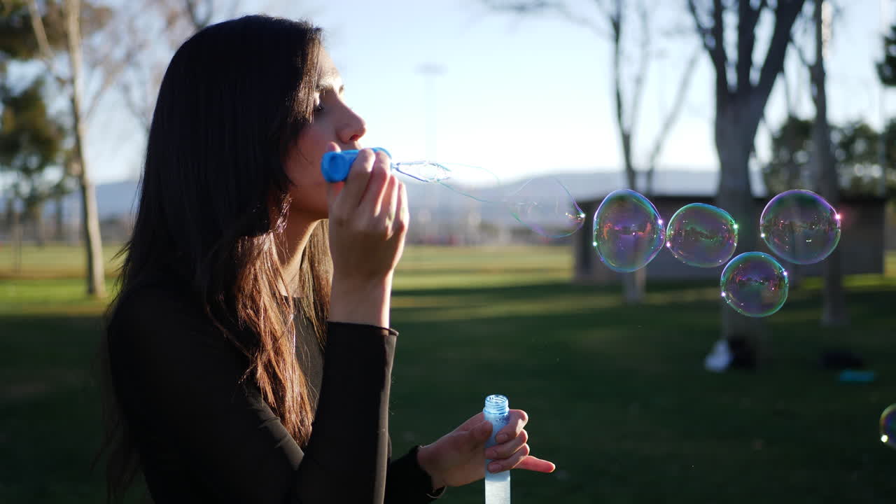 A happy young woman blowing iridescent bubbles and being playful and smiling outdoors in sunshine