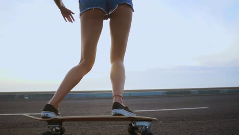 A-slow-motion-scene-captures-a-woman-skateboarding-on-a-road-at-sunset,-framed-by-mountains-and-a-beautiful-sky.-She's-wearing-shorts