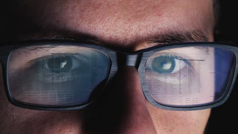 man works on computer screen, which is reflected on his glasses - code, numbers, network - close up