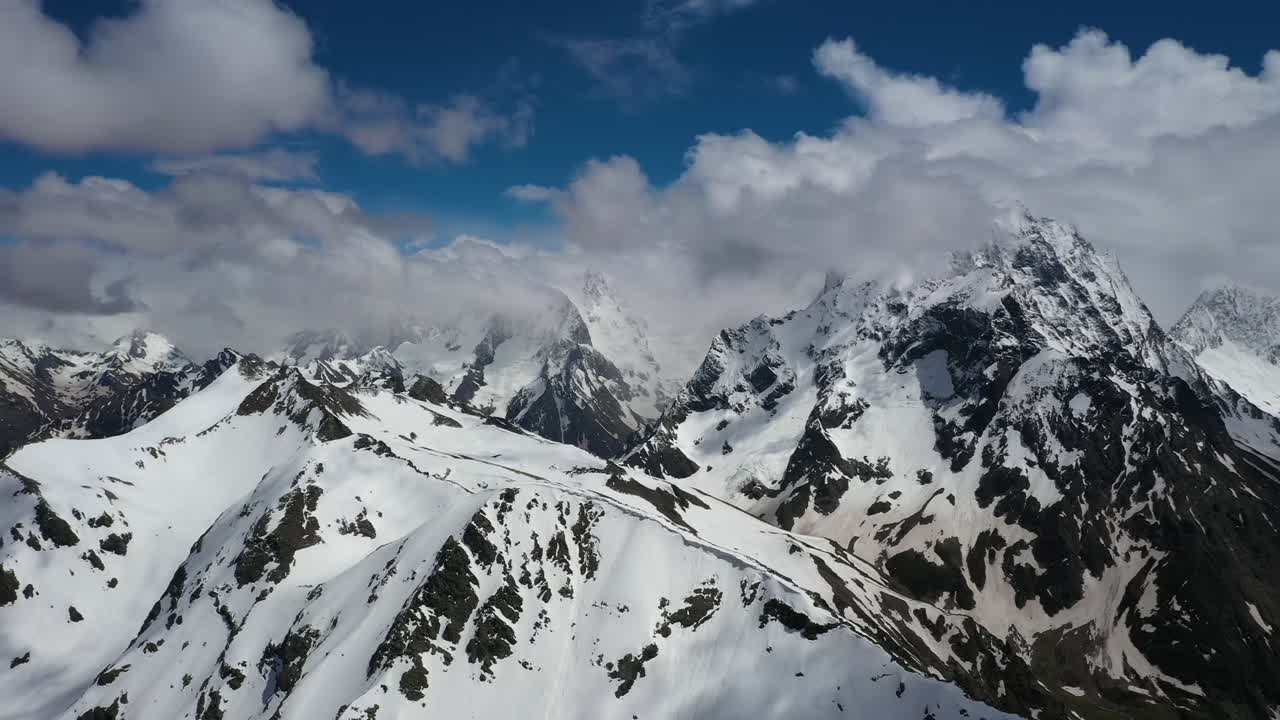 Volo aereo tra le nuvole di montagna sopra splendide vette innevate e ghiacciai.