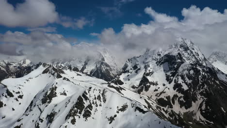 Air-flight-through-mountain-clouds-over-beautiful-snow-capped-peaks-of-mountains-and-glaciers.