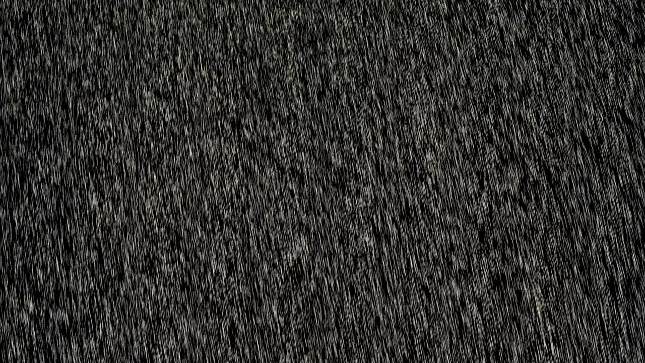 Heavy angled rain falling in front of the camera against black screen. Heavy rainstorm hitting black surface