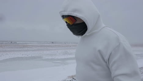 Man-in-Hoodie,-Snow-Goggles-and-Mask-Walking-on-Snowfall-on-Cold-Windy-Winter-Day