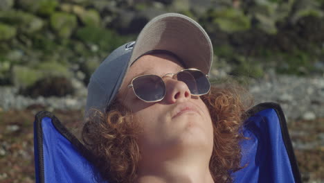 close up of male tourist in cap and sunglasses relaxing under the sunlight at the beach