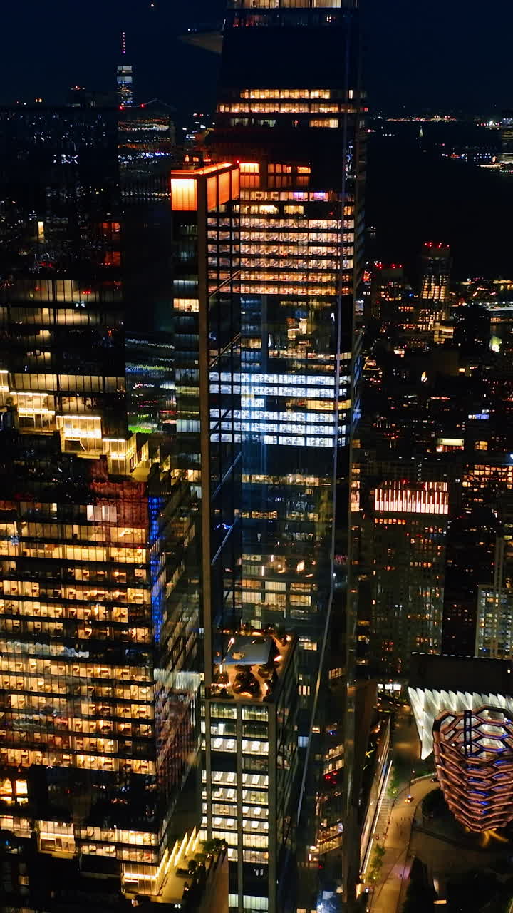 Light in the windows of beautiful skyscrapers at night. Drone footage descending above the sparkling cityscape. Vertical video