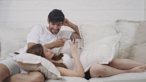행복한 중동 젊은 남성과 아시아 여성, 소셜 미디어에서 스마트폰을 사용하는 사람들, 집에서 사파에 앉아있는 사람들, 기술 장치의 라이프 스타일, 다민족