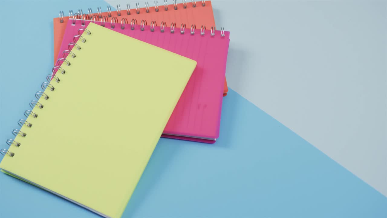 vista aérea de cuadernos de colores sobre fondo azul, en cámara lenta