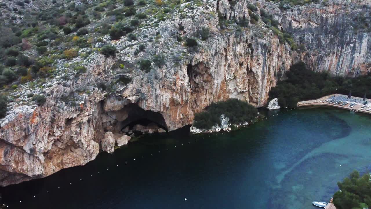 Ripresa orbitale del lago sommerso di Vouliagmeni ad Atene, Grecia, con scogliere e grotte circostanti | 4K