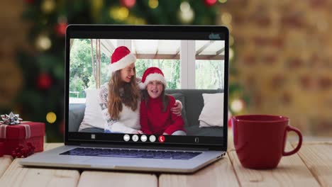 Happy-mother-and-daughter-in-santa-hats-on-video-call-on-laptop,-with-christmas-decorations