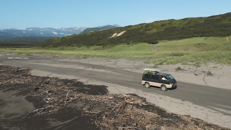 Campervan-driving-along-coastal-route-of-grass,-soil-and-wet-sand