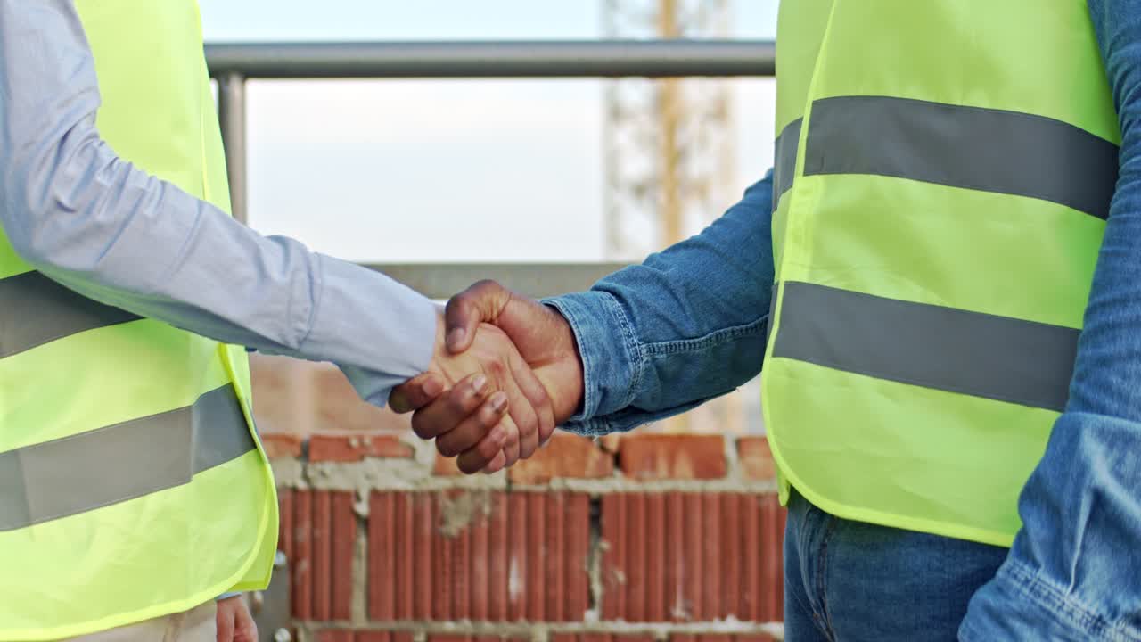 primer plano de la mano del hombre afroamericano y la mano de la mujer caucásica estrechando la mano en el sitio de construcción.