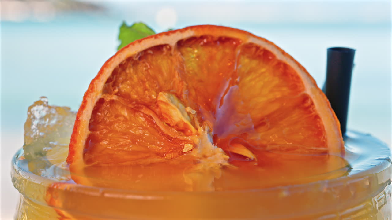 Close up of an orange cocktail on a table with a blurred view of the sea on the background