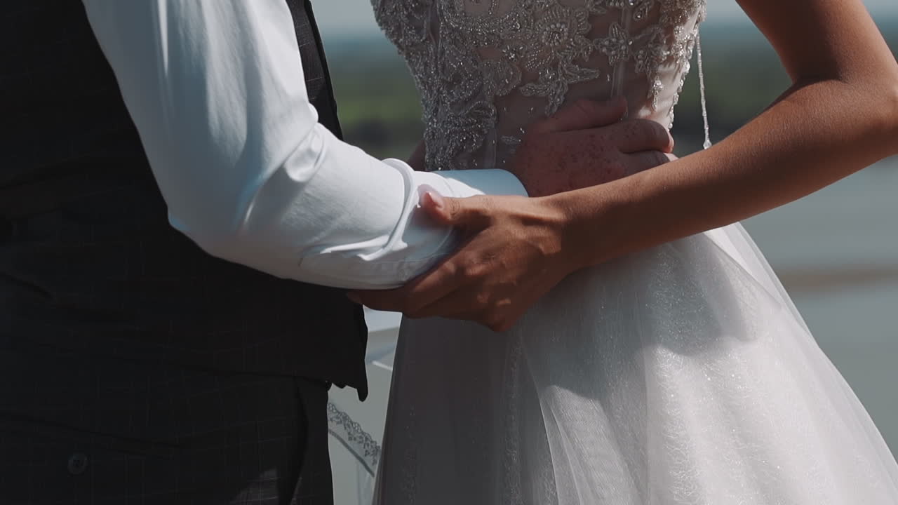 Newlywed groom holds waist of young wife in white dress