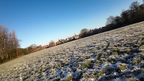 FPV-flying-frosty-winter-sunlit-meadow-during-golden-hour-sunrise,-Low-angle