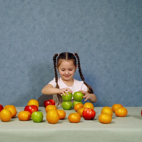 cheerful little girl playing with ripe fruits on the table. happy child building a tower with fresh organic apples. healthy fruits full of vitamins on the table.