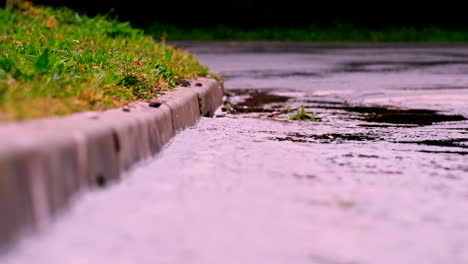 Escorrentía-De-Agua-De-Lluvia-Cuesta-Abajo-Hacia-El-Drenaje-De-La-Calle-De-Hormigón,-Toma-De-Teleobjetivo