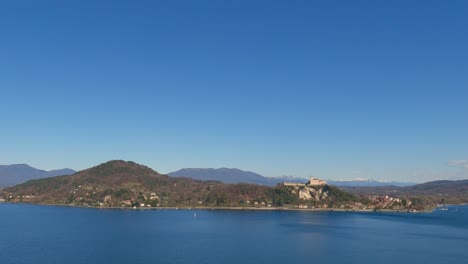 Panoramic-view-of-beautiful-lake-Maggiore-and-Angera-fortress-with-clear-sky-and-boat-sailing-over-calm-waters