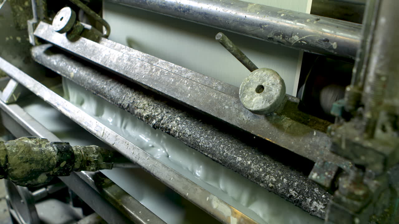 Close shot of an old and well-worn machine printing green wallpaper, using a tray of liquid light green paint.