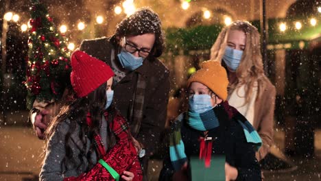 close-up view of caucasian happy family wearing facial masks holding presents on the street while it¬¥s snowing in christmas