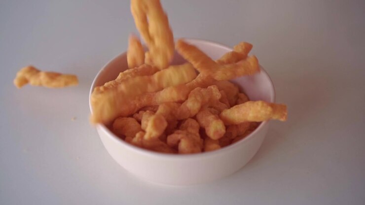 Golden fried snack pieces dropping into a bowl on a kitchen counter. Comfort food, crunchy treat and snacking concept background.