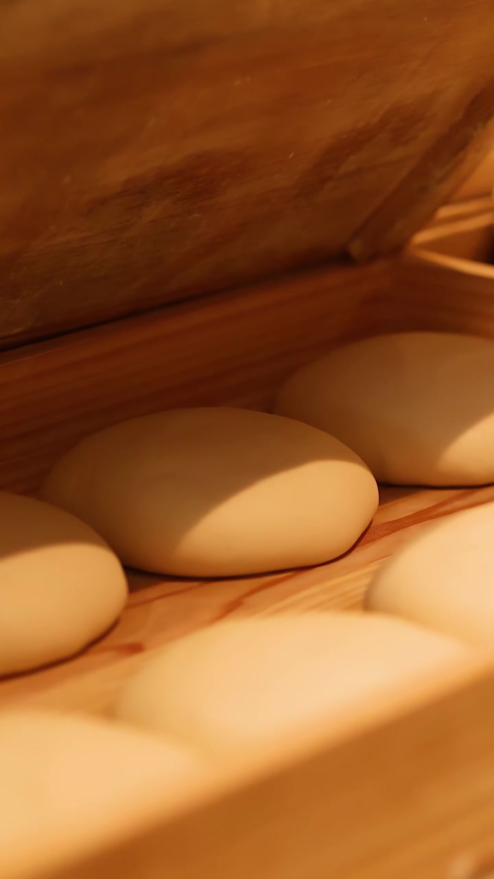 Close-up shot of hands closing a wooden proofing box filled with round pizza dough balls.