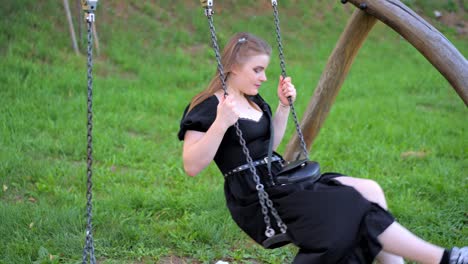 young girl in a long black dress is smiling while swinging on a swing