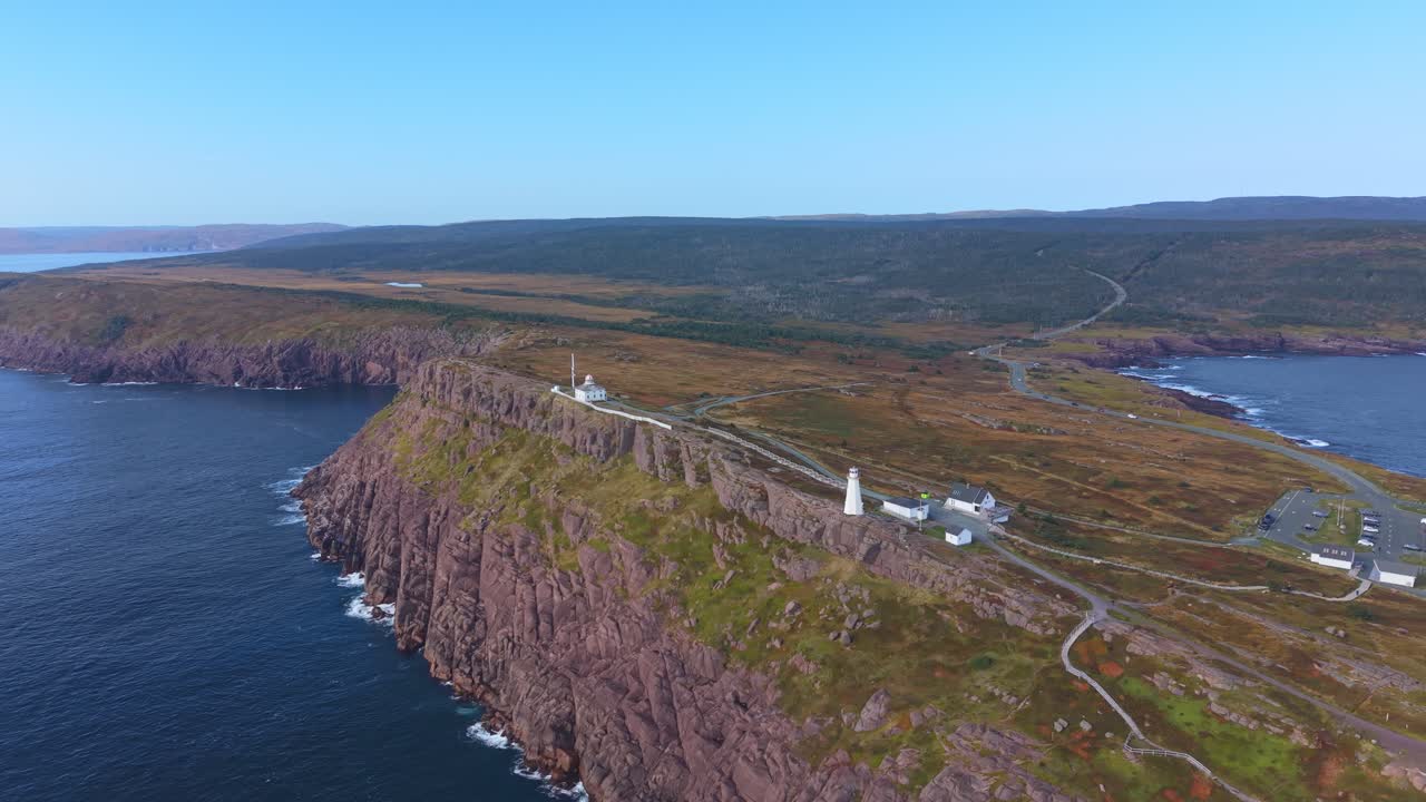 A low-angle aerial shot glides along the dramatic cliffs of Cape Spear, showing coastal bluffs and a distant view of Signal Hill, filmed from outside the national park boundary
