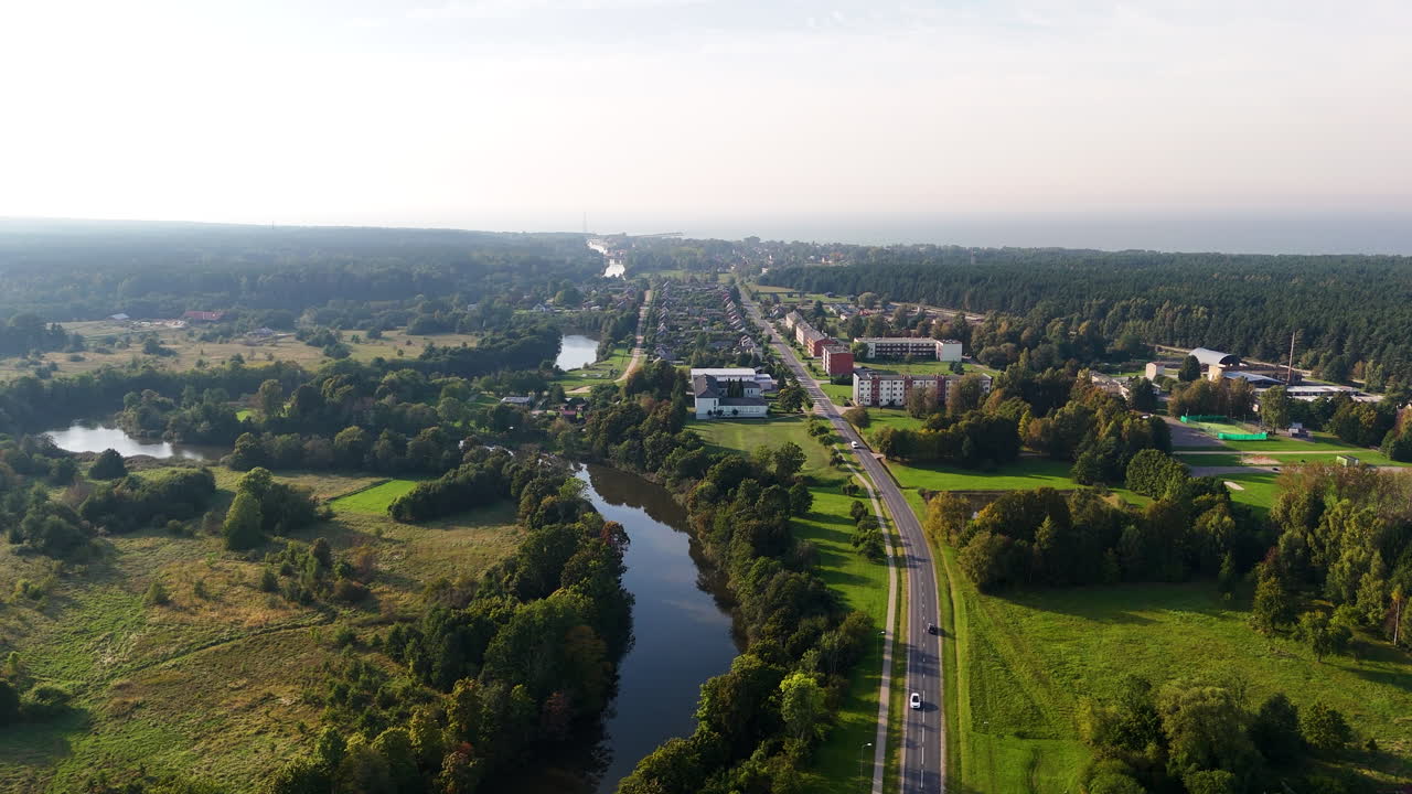 Aerial video of rural approach to Pavilosta town with river and forest by the coast.