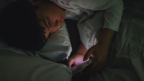niño joven en el dormitorio en casa acostado en la cama usando el teléfono móvil para enviar mensajes de texto por la noche 5
