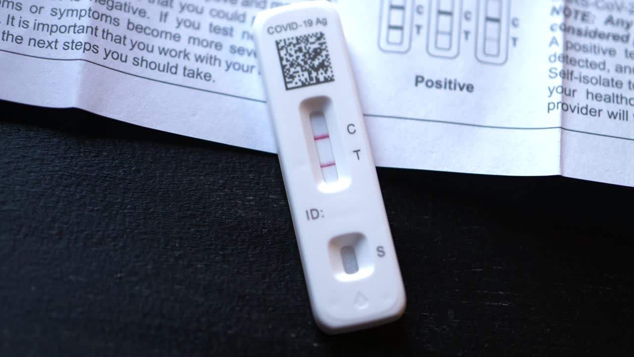 Covid 19 positive at home antigen test kit on black table with instruction book showing how to find positive results with two red lines close shot slowly dollying in