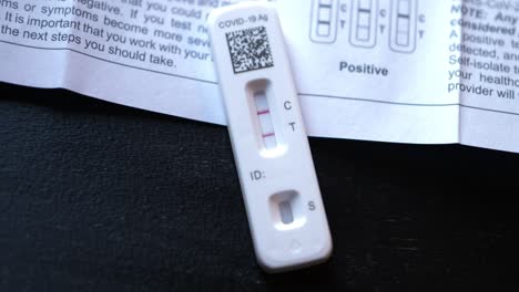 Covid-19-Positives-Zu-Hause-Antigen-Testkit-Auf-Schwarzem-Tisch-Mit-Anleitungsbuch,-Das-Zeigt,-Wie-Man-Positive-Ergebnisse-Findet,-Mit-Zwei-Roten-Linien-In-Der-Nähe,-Die-Langsam-Hereinrollen