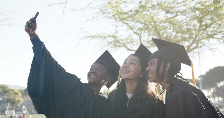 Studenti afroamericani, lo studente a sinistra alza il telefono, posando sul campo per la laurea con i tocco.