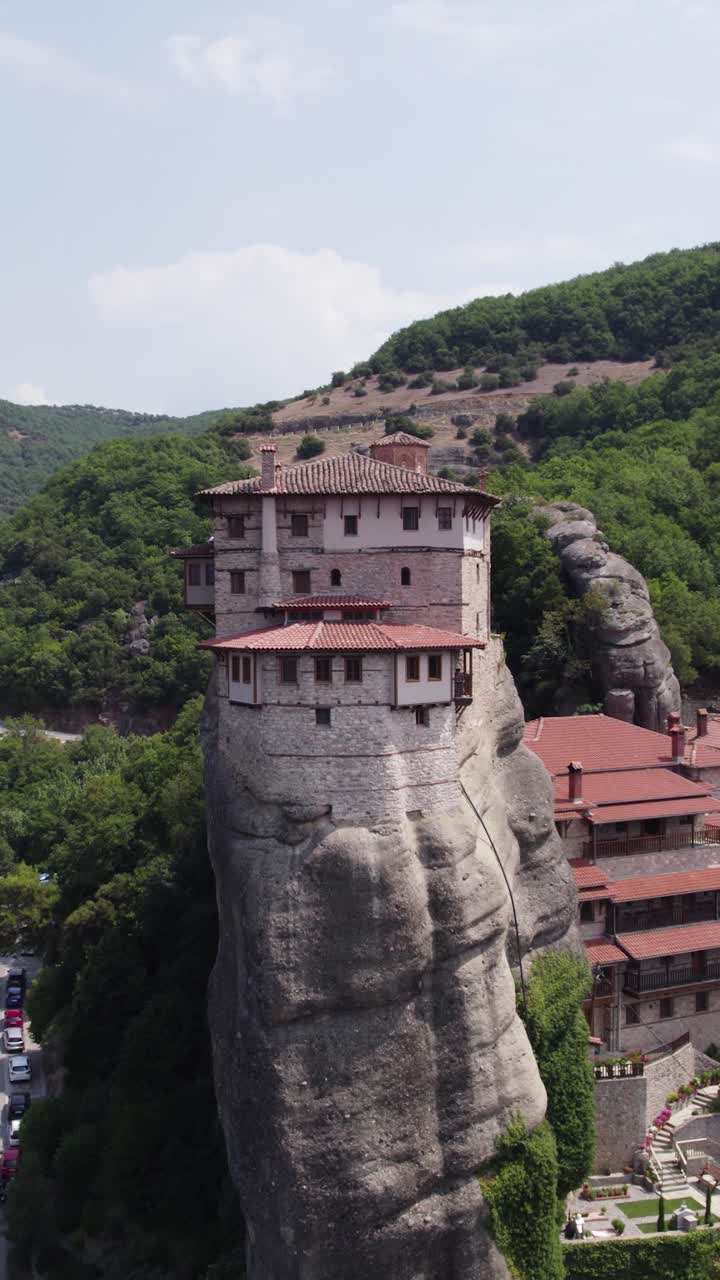 Vertical aerial pullback establishing St. Rousanou Monastery atop a cliff in Meteora, Greece