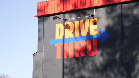 Señalización-Pintada-De-Naranja-&quot;drive-Thru&quot;-Pintada-En-La-Pared-De-Un-Edificio-En-Gris-Y-Una-Flecha-Que-Apunta-Hacia-La-Derecha-En-La-Dirección-De-Conducción