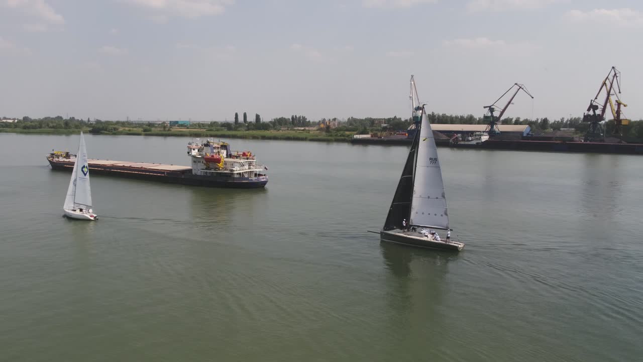 yate de vela en el río con buques de carga