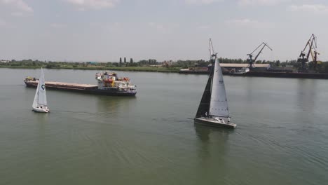 yate de vela en el río con buques de carga