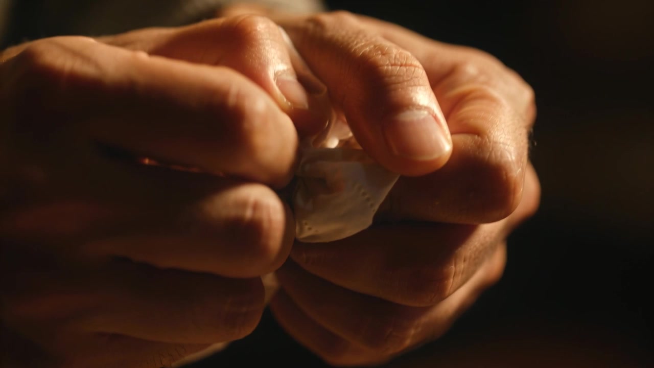 Mani che pizzicano e strizzano un cuscinetto perforato in una luce calda, spremendo l'umidità, con un anello visibile.