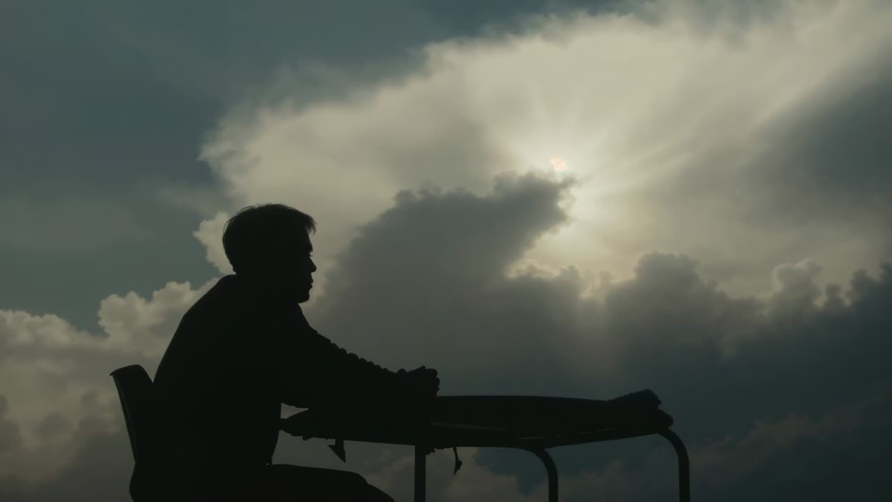 Shifting sunlight under cloudy sky causing seated man leaning forward on gurney jacket, copy space