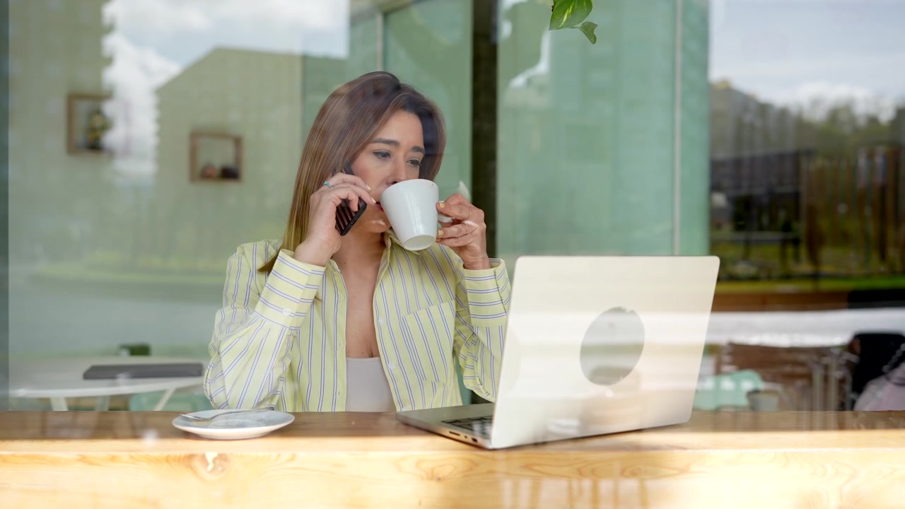 Joven hablando por teléfono y trabajando en su laptop en un café