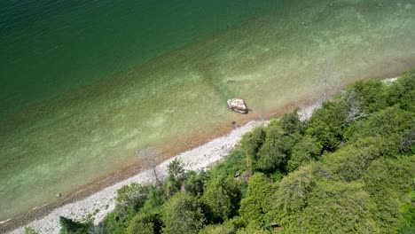 Aerial-descent-of-forested-coastline-and-large-rock,-Lake-Huron,-Michigan