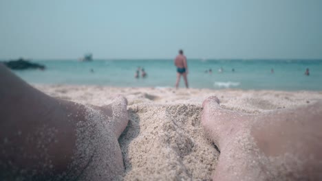 close person legs near endless ocean with swimming people