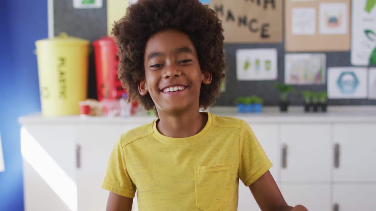 African american schoolboy standing, smiling in classroom looking at camera learning about recycling