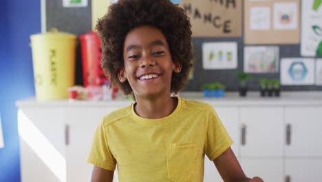 African-american-schoolboy-standing,-smiling-in-classroom-looking-at-camera-learning-about-recycling