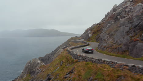 Car-driving-on-narrow-road-winding-along-rocky-slope-high-above-sea-coast.-Breath-taking-ride-on-panoramic-route.-Ireland