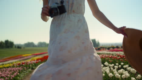 Young-woman-with-camera-and-straw-hat-turning-around-in-beautiful-tulips-garden.